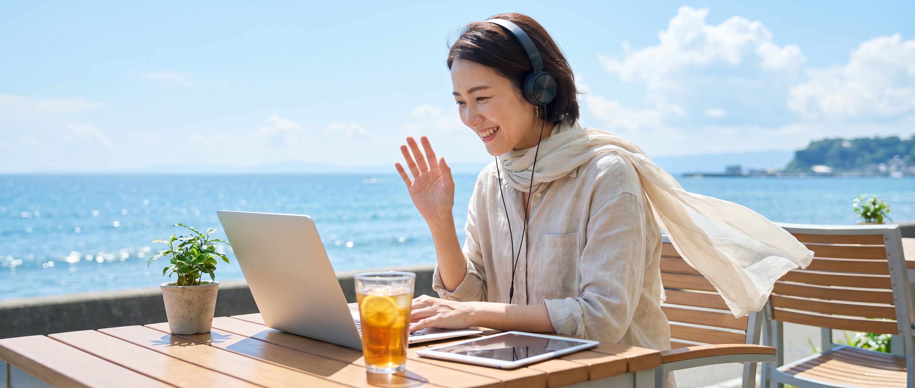 夏の海辺のテラスでオンライン語学レッスンを楽しむ女性